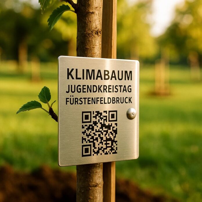 Brucker Blatt - Nahaufnahme eines jungen Baumes mit einem rechteckigen, silberfarbenen Schild, das mit einem Niet an einem Holzpfahl befestigt ist. Auf dem Schild steht in schwarzer Schrift 
